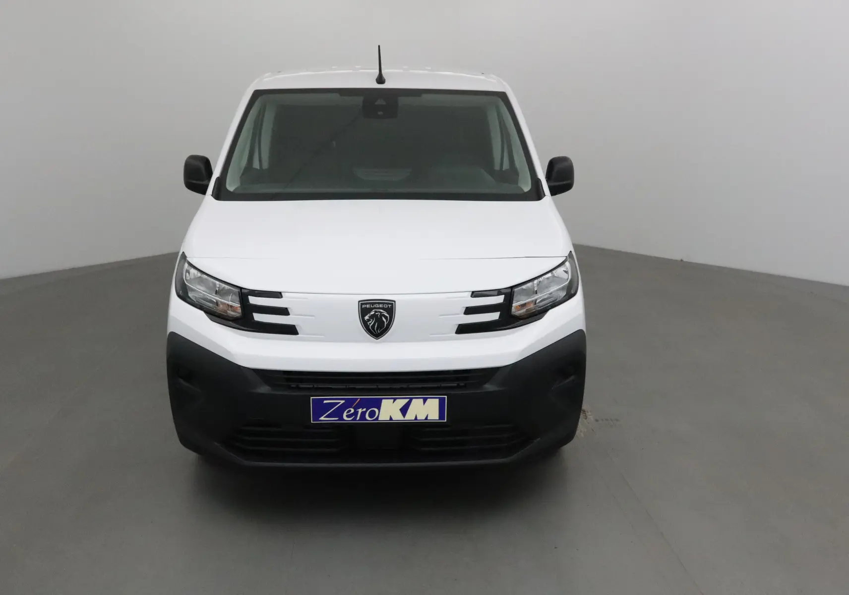 Vue frontale d'un utilitaire Peugeot Partner blanc avec calandre noire et logo lion central, sur fond neutre gris.