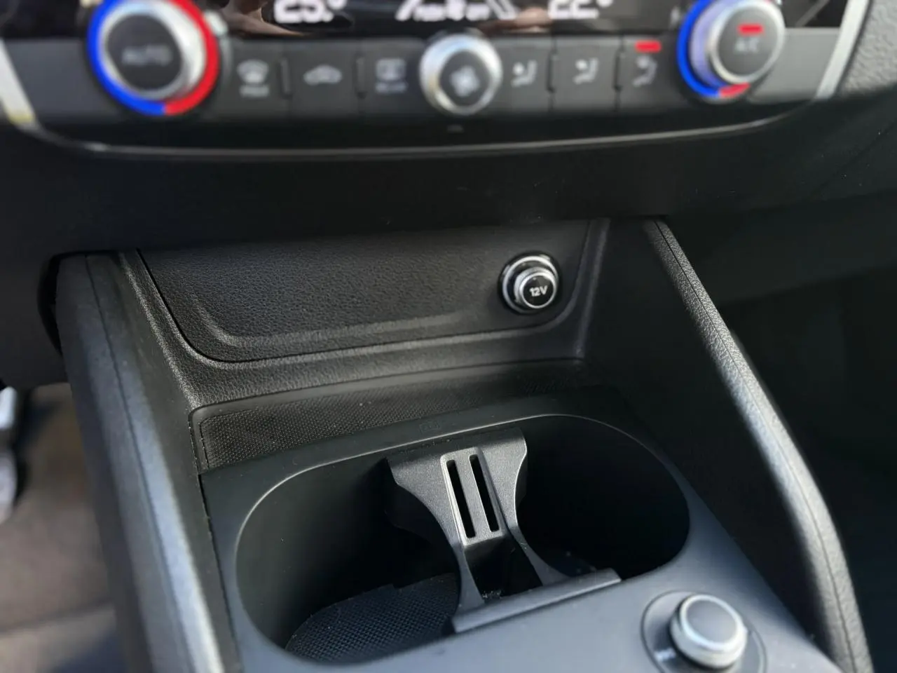 Gros plan sur la console centrale de l'Audi Q2 30 TDI S-Line 2025, montrant les commandes de climatisation et un port 12V.