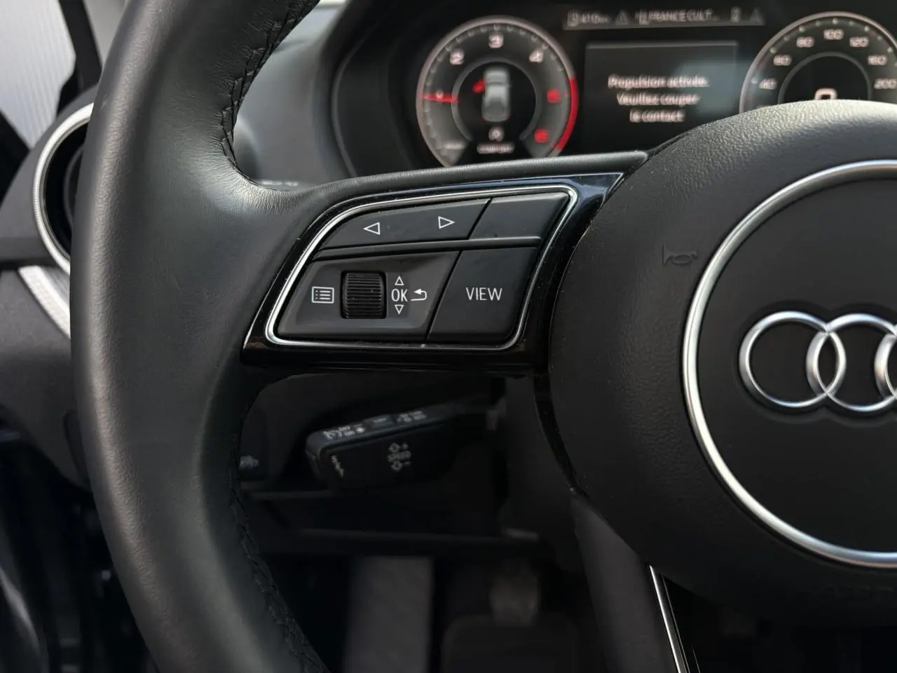 Gros plan sur le volant cuir multifonction noir de l'Audi Q2 30 TDI S-Line avec commandes intégrées et tableau de bord partiellement visible.