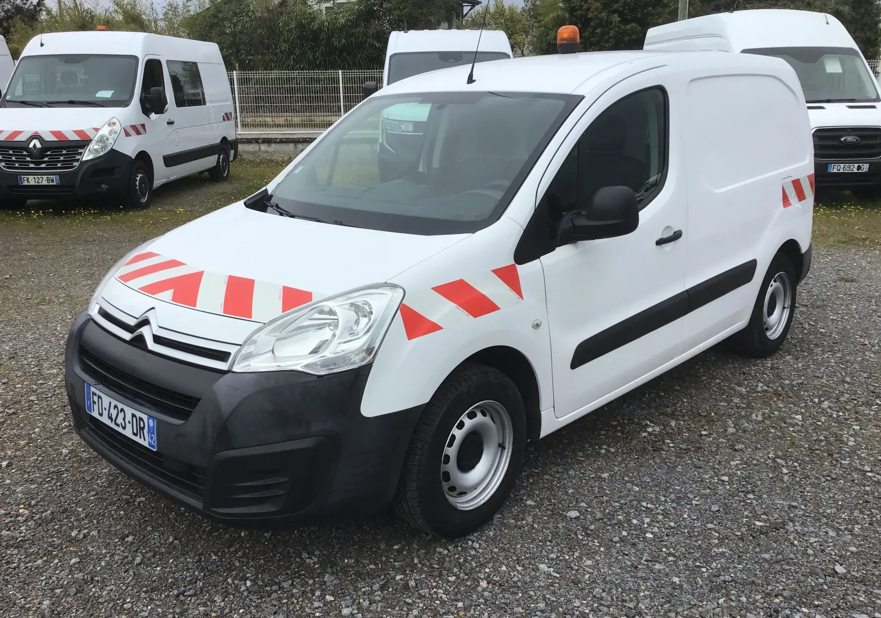 Vue 3/4 avant d'un Citroën Berlingo blanc 2019 avec bandes rouges réfléchissantes et gyrophare orange sur le toit.