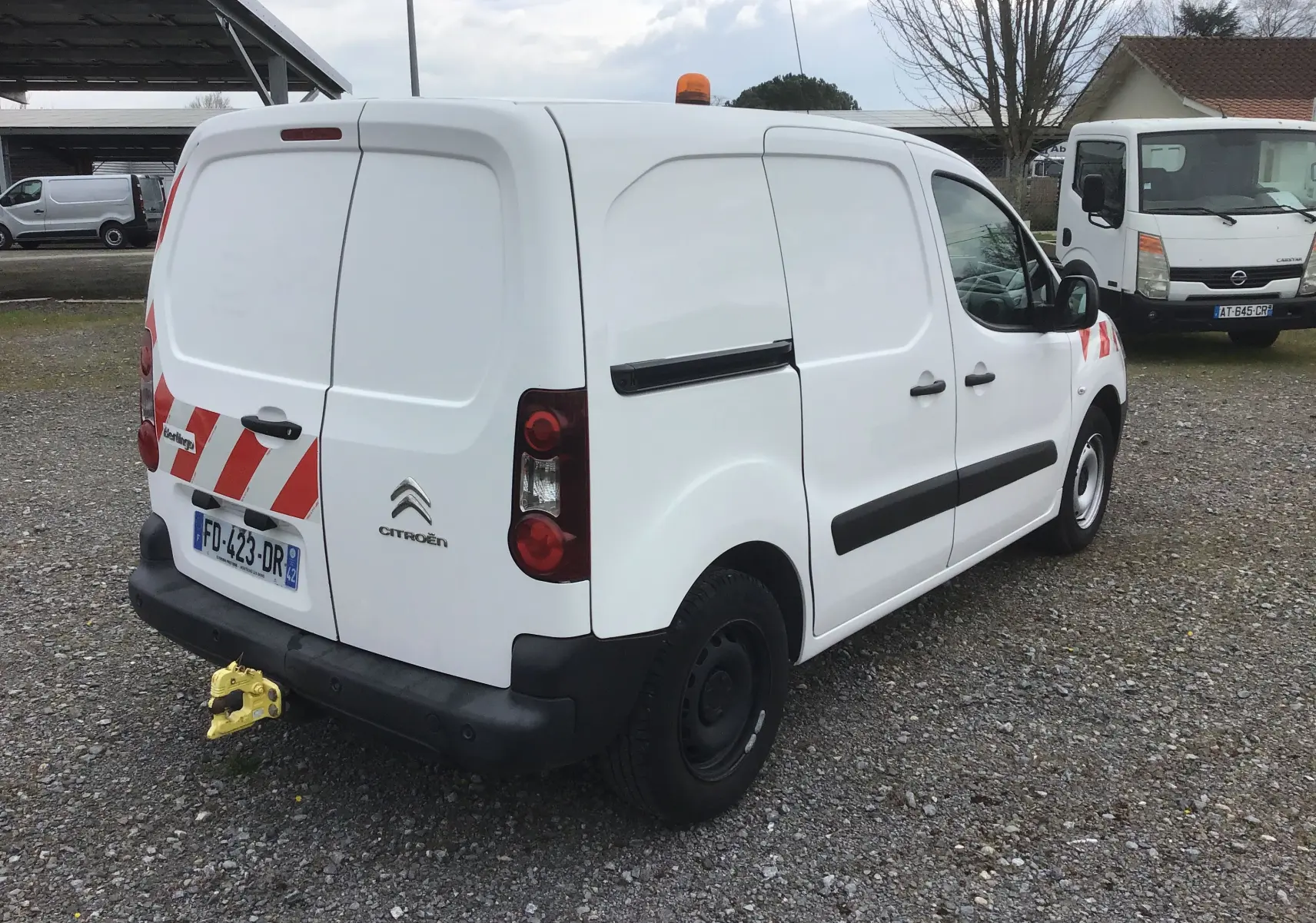 Vue 3/4 arrière droite d’un Citroën Berlingo blanc utilitaire avec bandes rouges réfléchissantes et gyrophare orange.