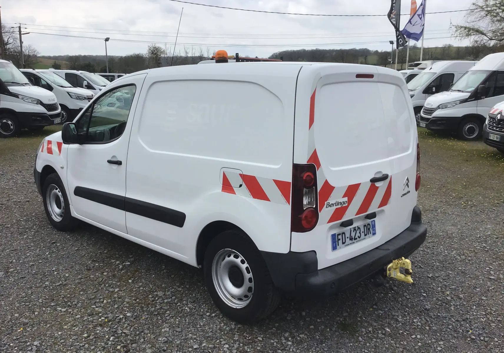 Vue 3/4 arrière droite d'un Citroën Berlingo blanc utilitaire avec bandes rouges réfléchissantes et attelage jaune.
