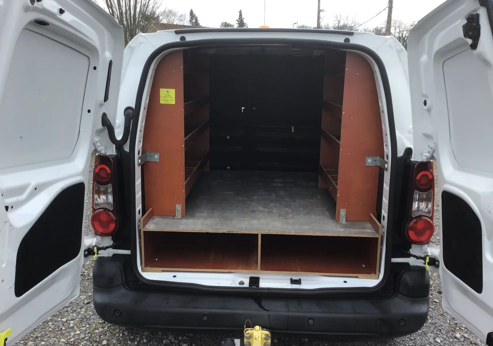 Vue arrière ouverte d’un Citroën Berlingo blanc 2019 avec étagères en bois dans l’espace de chargement.