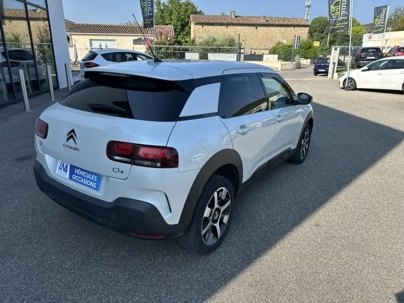 Vue 3/4 arrière droite d'une Citroën C4 Cactus blanche 2018 avec toit noir et protections noires sur les bas de caisse.