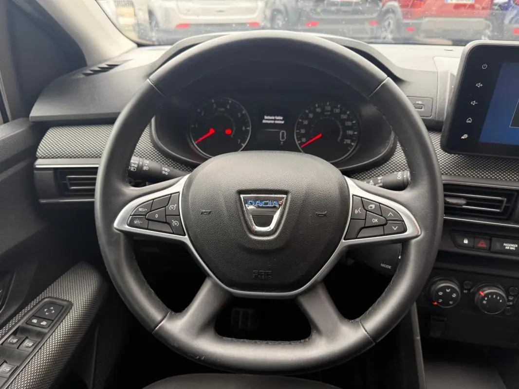 Vue rapprochée du volant noir du Dacia Sandero 2021 avec commandes intégrées et tableau de bord digital.