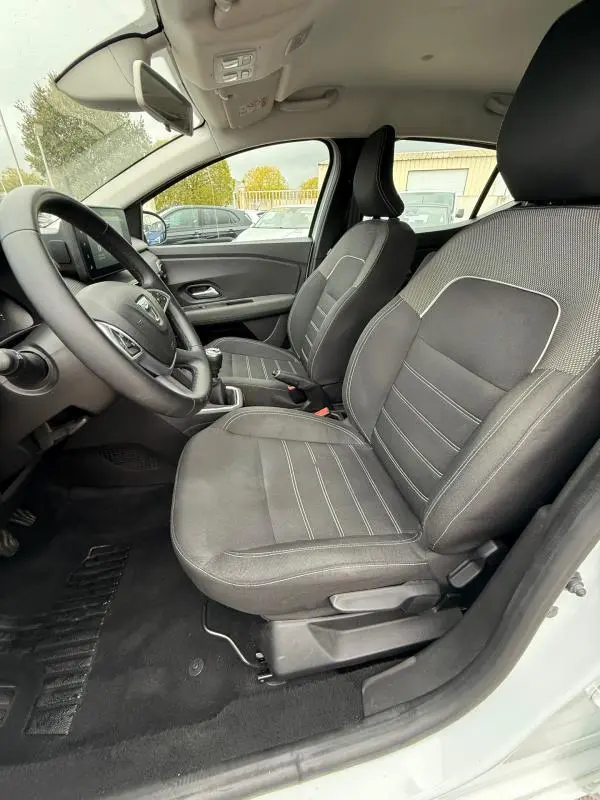 Vue intérieure côté conducteur de la Dacia Sandero blanche 2021, sièges noirs avec surpiqûres claires et volant réglable.