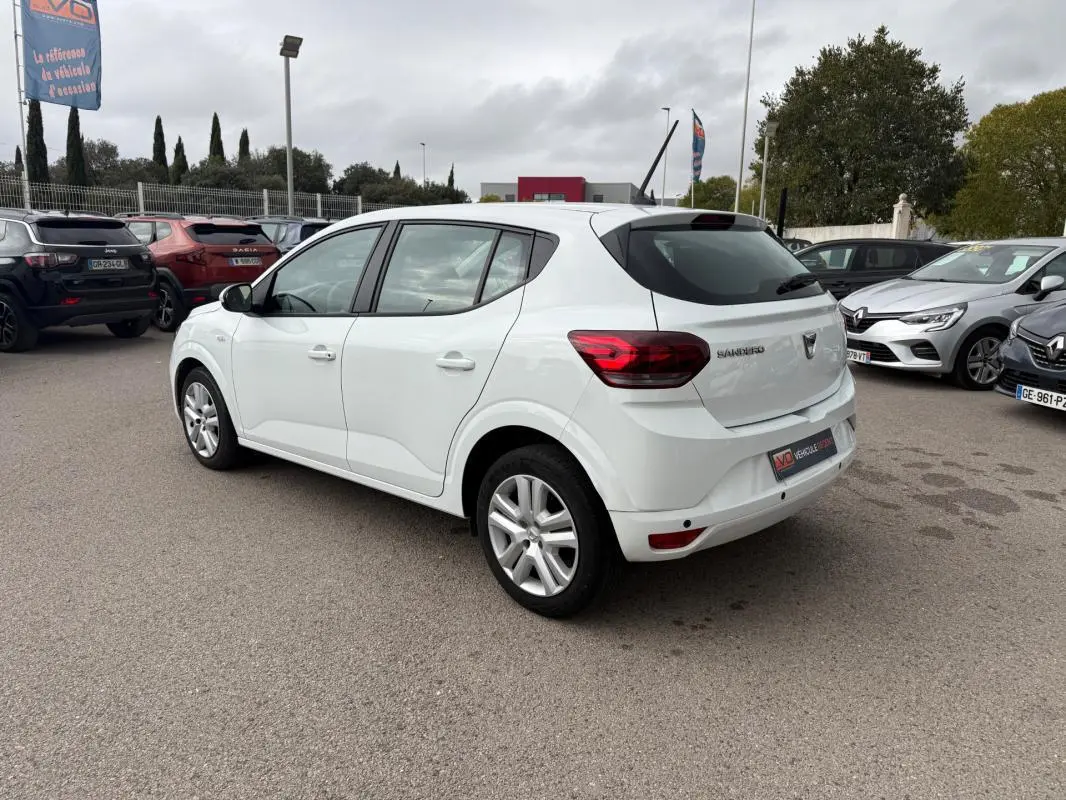 Vue 3/4 arrière droite d'une Dacia Sandero blanche 2021 avec vitres surteintées et feux arrière allumés.
