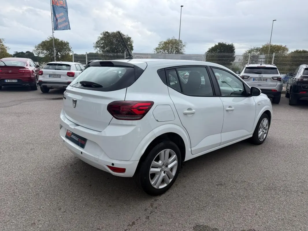 Vue 3/4 arrière droite d'une Dacia Sandero blanche 2021, avec feux arrière distinctifs et vitres surteintées.