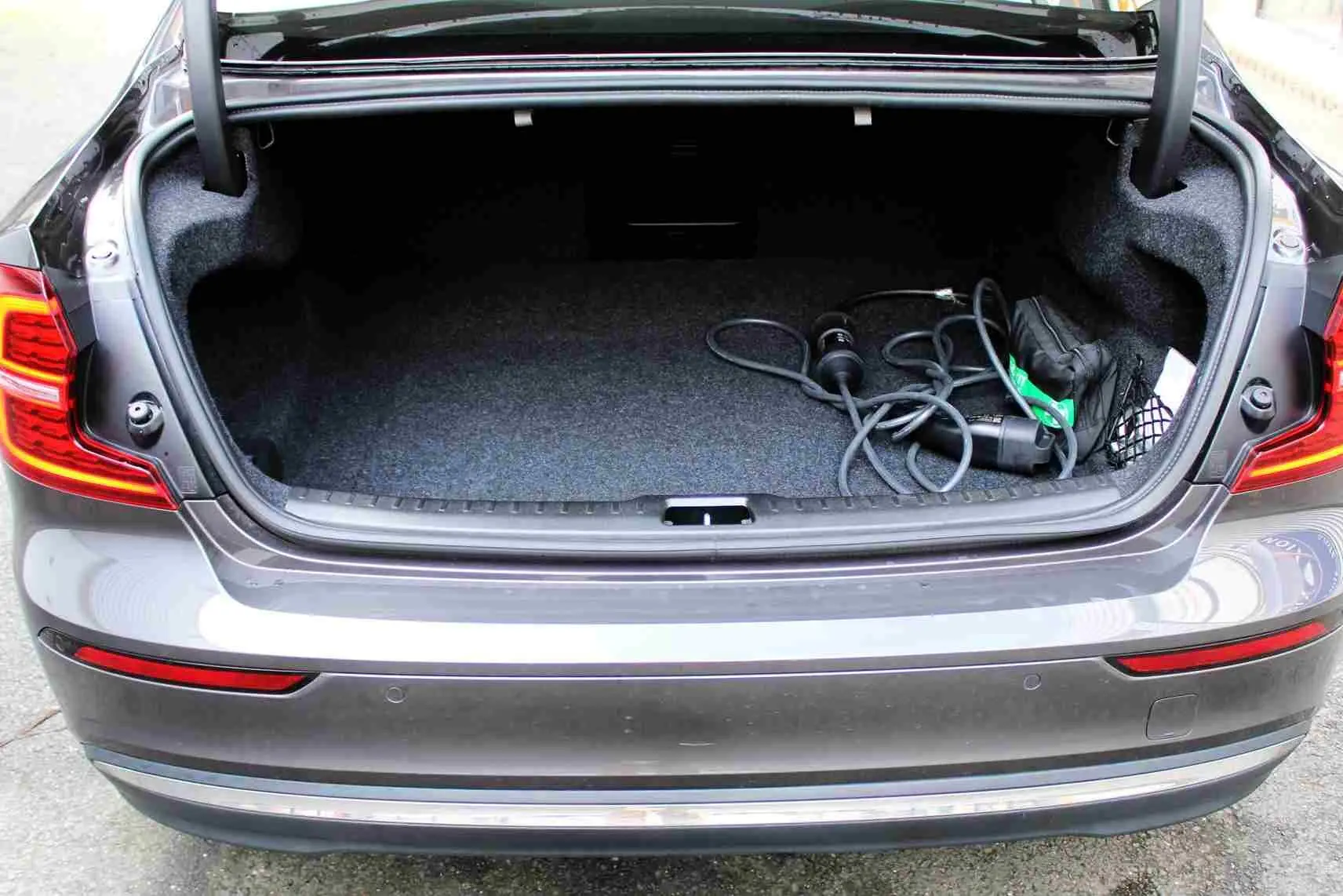 Coffre ouvert vu de l'arrière d'une Volvo S60 T6 hybride rechargeable gris métal avec câble de recharge visible.