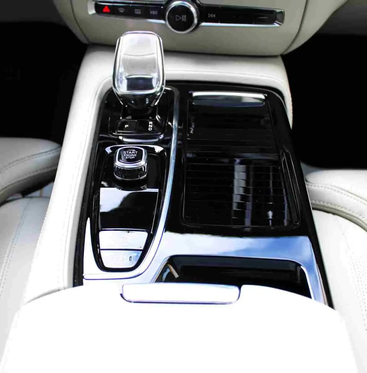 Vue rapprochée de la console centrale noire brillante avec levier de vitesse cristal et sièges cuir clair d'une Volvo S60 2024.