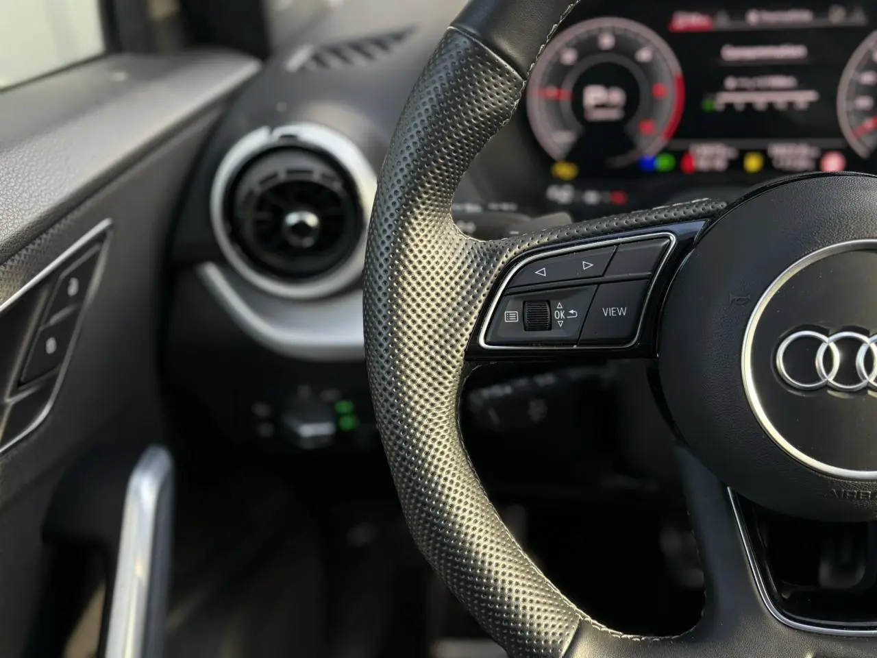 Gros plan sur le volant cuir perforé à 3 branches et le tableau de bord numérique de l'Audi Q2 35 TDI 150 S-Line 2025.