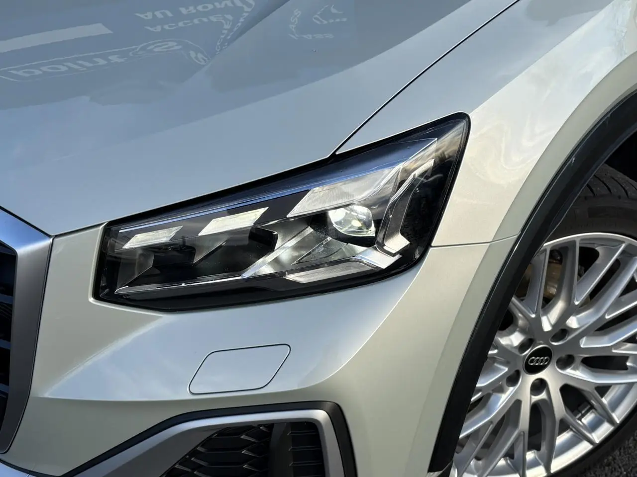 Gros plan sur le phare avant droit et la roue argentée d’un Audi Q2 35 TDI S-Line couleur argent rosé.