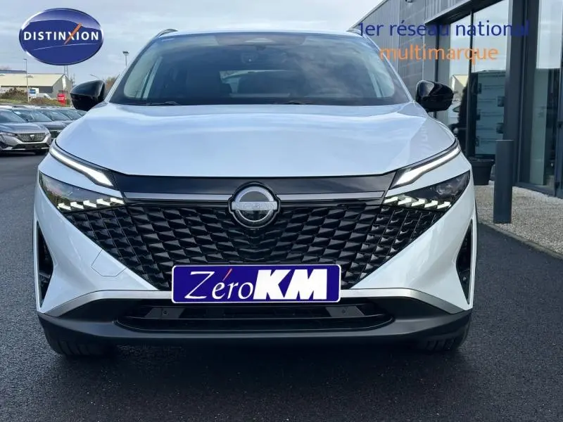 Vue avant du Nissan Qashqai Hybrid e-POWER blanc nacré 2025 avec calandre noire et feux LED distinctifs allumés.