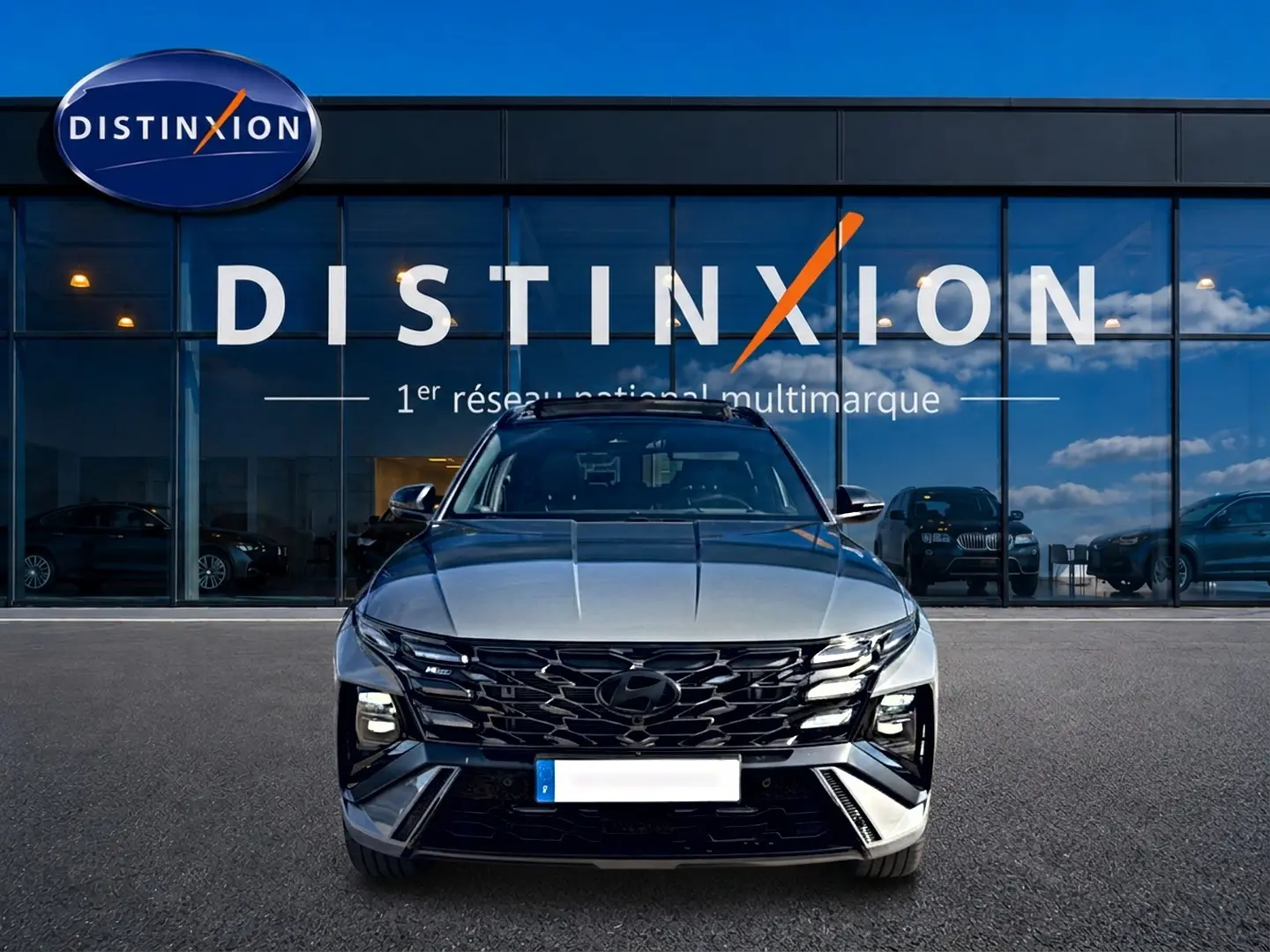 Vue avant d'un Hyundai Tucson 2026 gris shadow avec calandre noire et phares LED, devant une vitrine Distinxion.