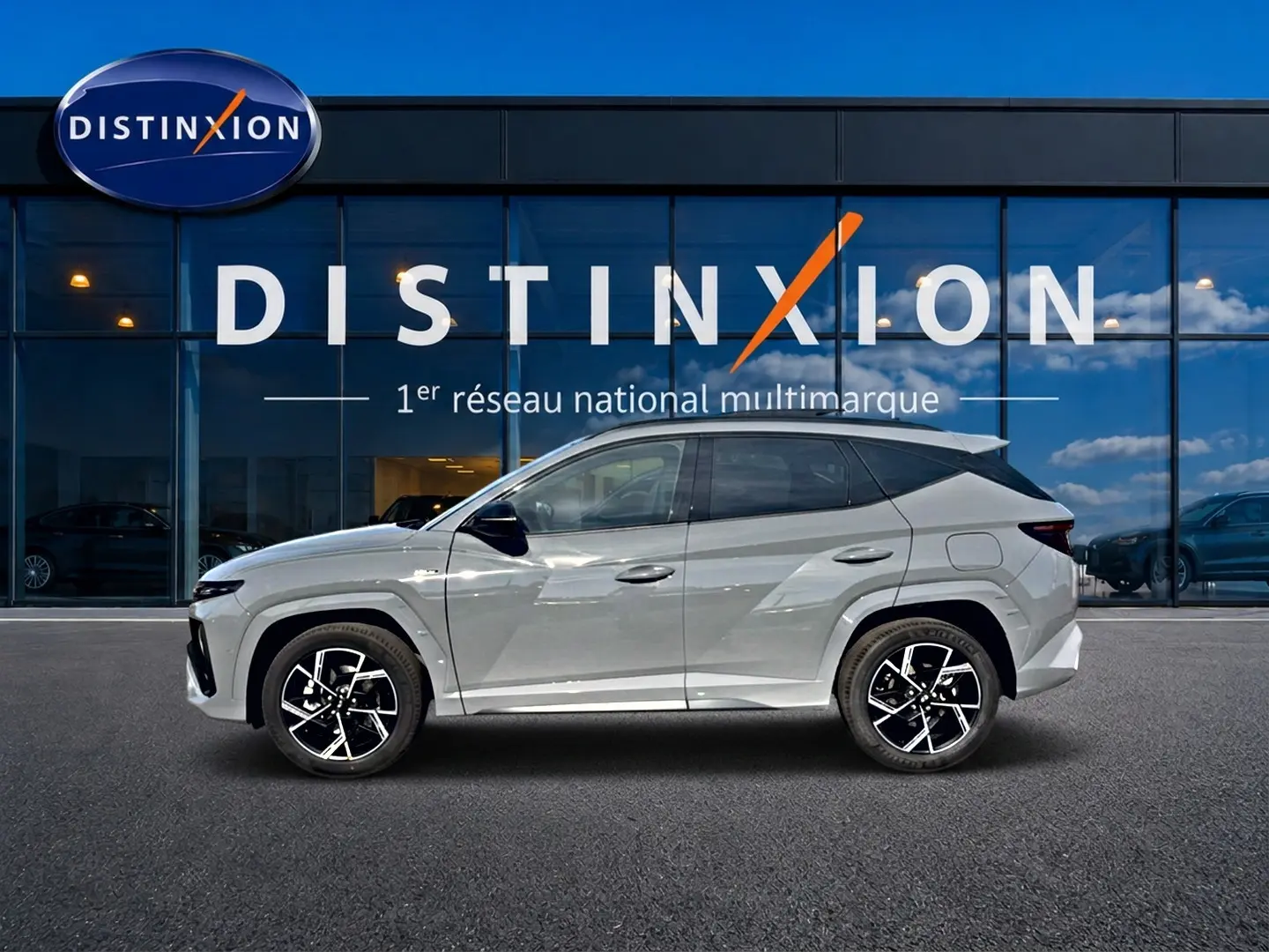 Vue de profil côté gauche du Hyundai Tucson 2026 gris shadow avec jantes alliage distinctives devant une vitrine Distinxion.