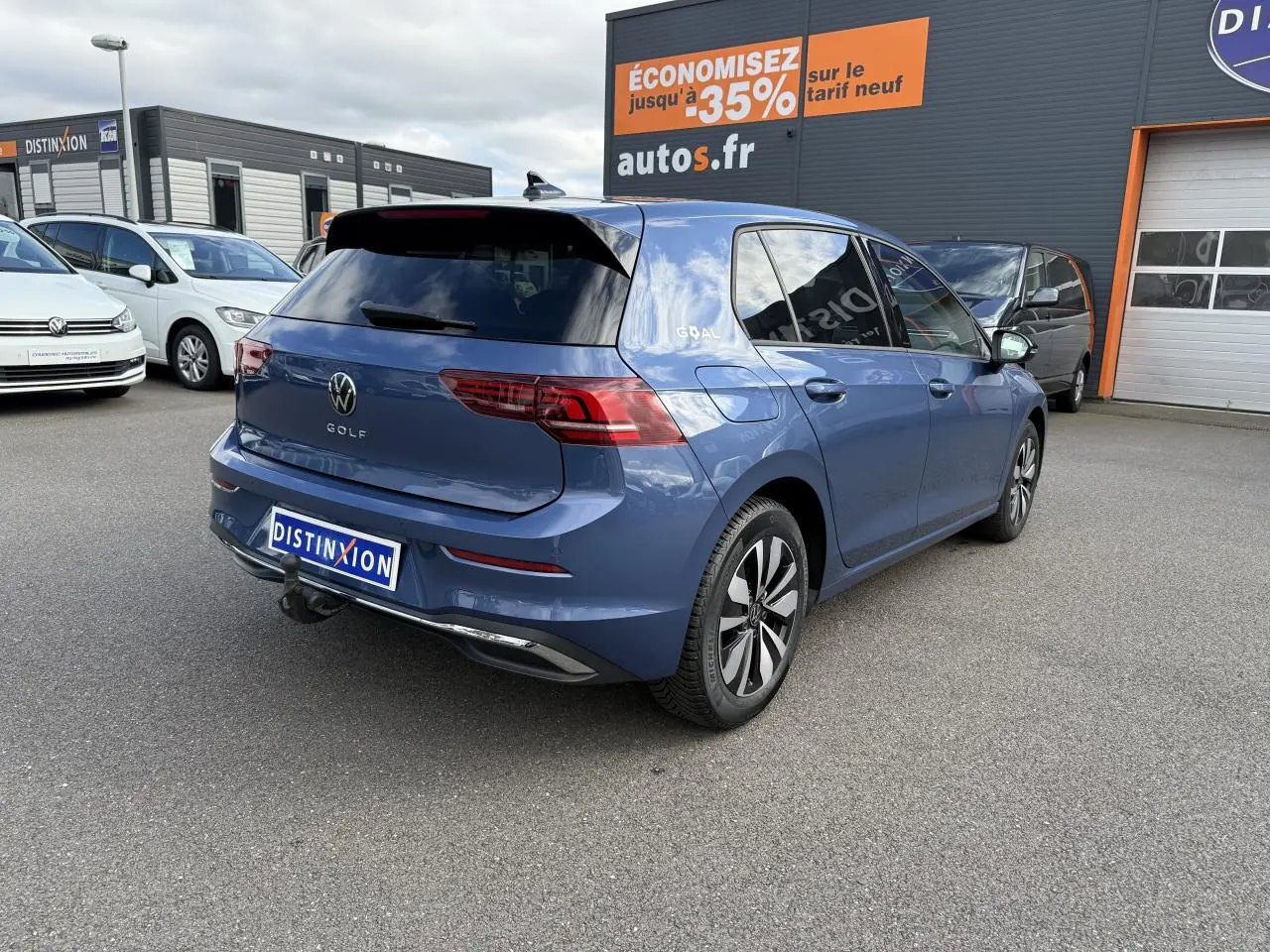 Vue 3/4 arrière droite d'une Volkswagen Golf bleu anémone métallisée avec attelage escamotable sur parking extérieur.