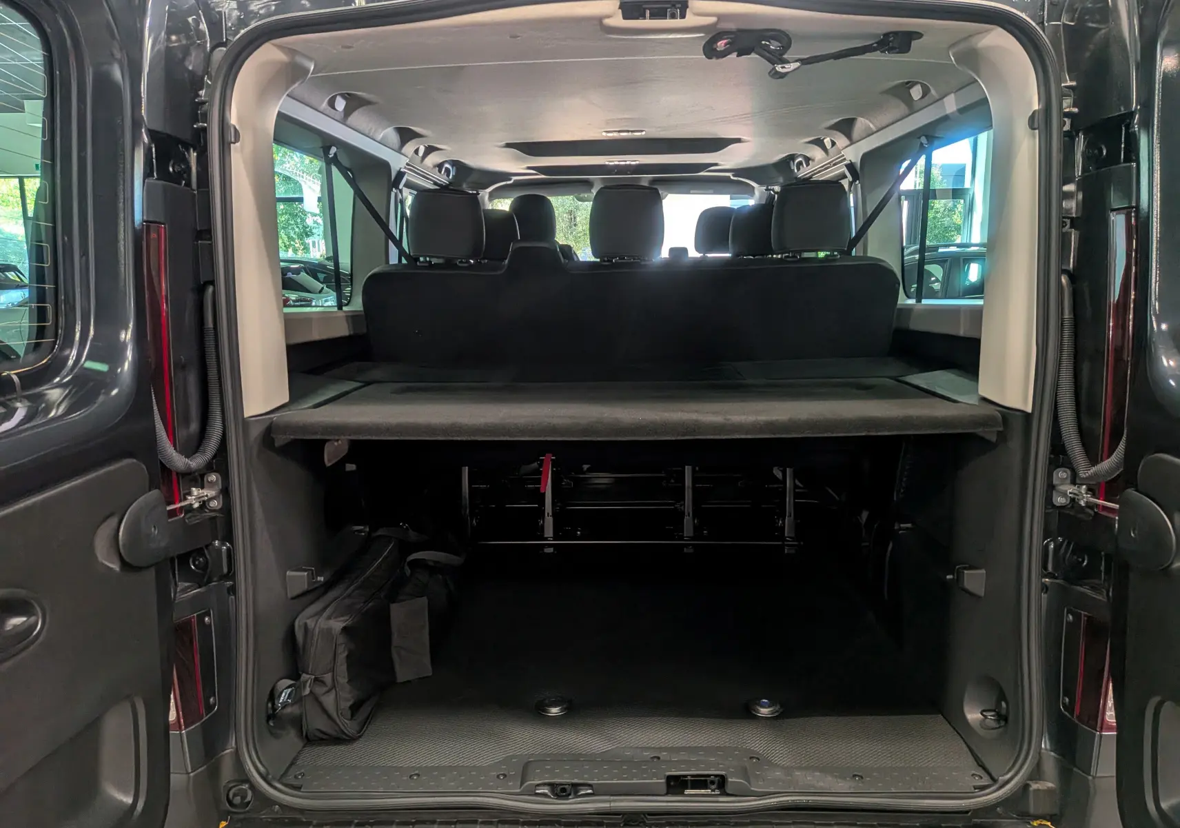 Vue arrière ouverte du Renault Trafic Combi gris comète montrant l'espace de chargement et les sièges arrière noirs.