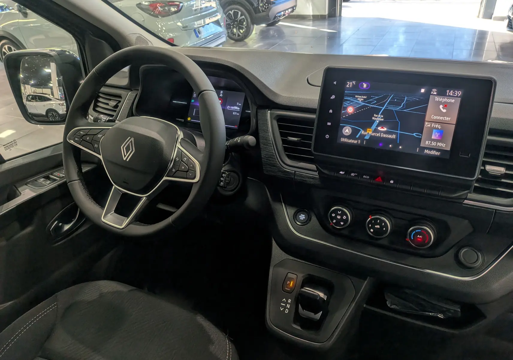 Vue intérieure du poste de conduite du Renault Trafic Combi 2025 avec tableau de bord noir et écran tactile central.