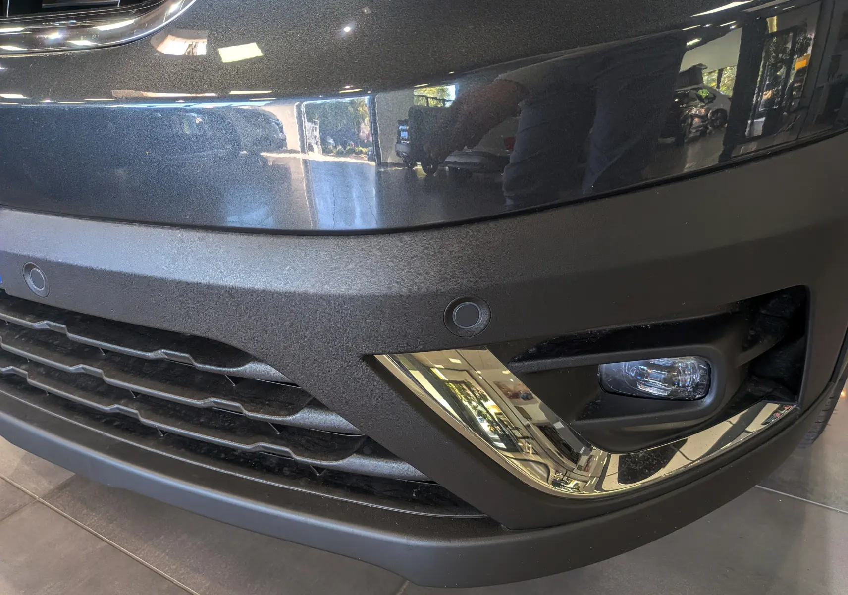 Gros plan sur le pare-chocs avant gris comète du Renault Trafic Combi avec antibrouillard et capteurs de stationnement.