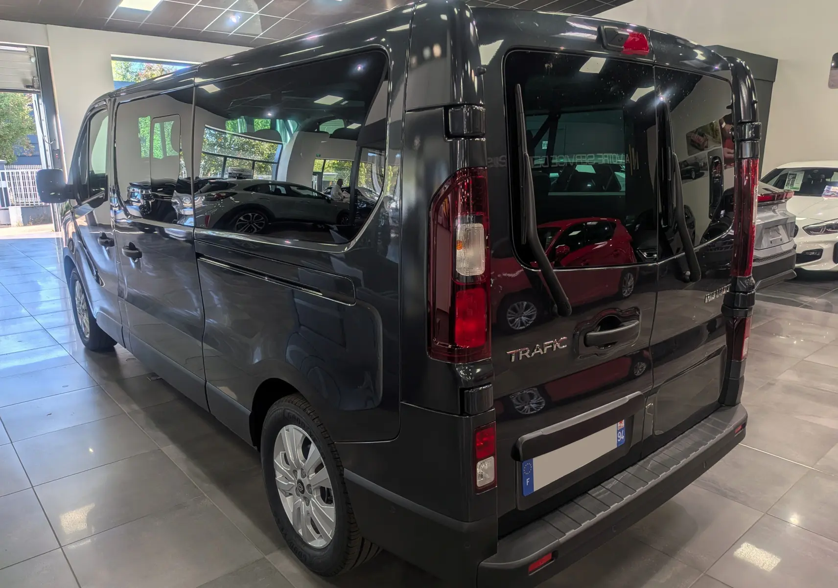 Vue 3/4 arrière droite du Renault Trafic Combi gris comète 2025 en showroom avec vitres teintées et hayon vitré.