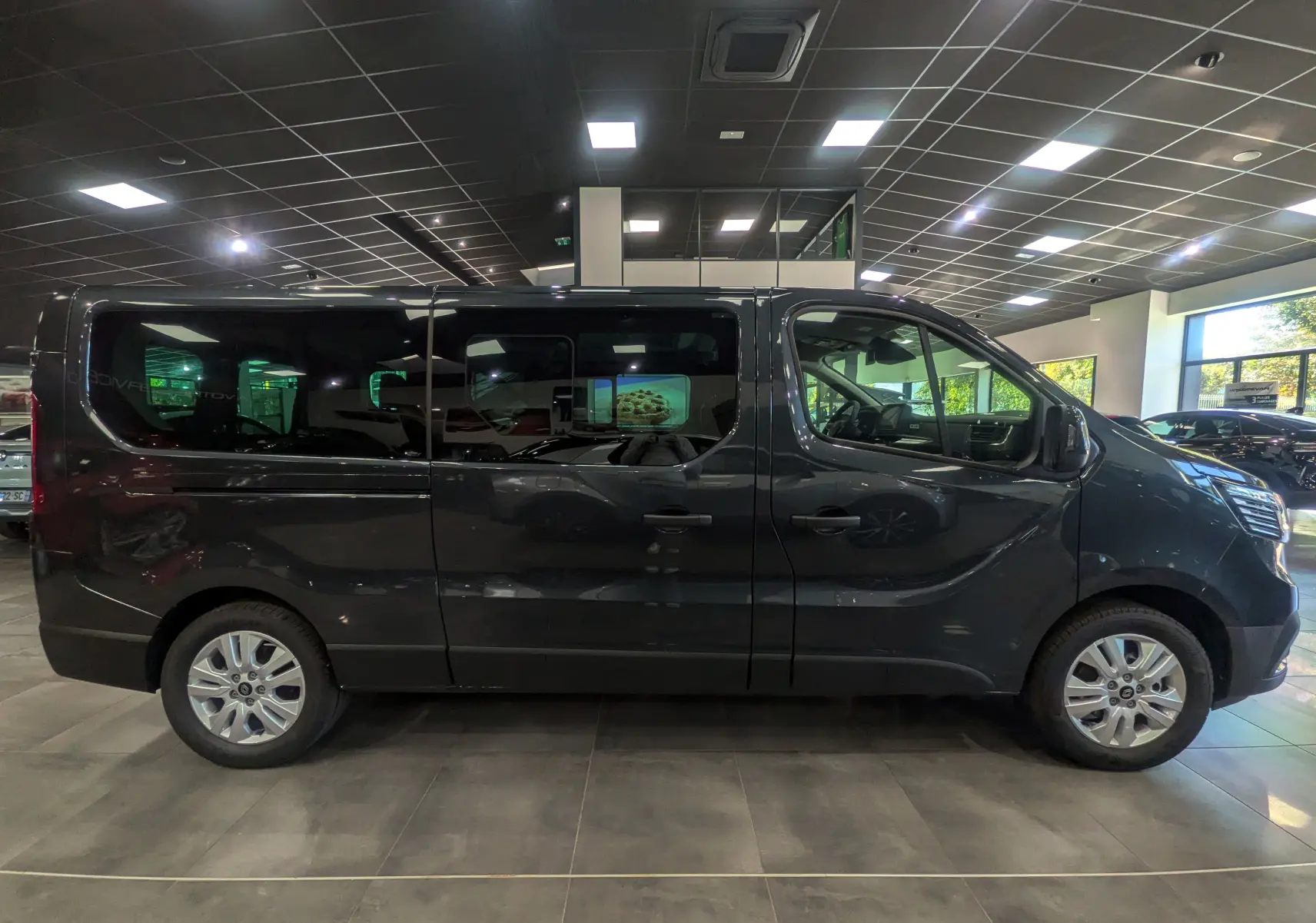 Profil droit d'un Renault Trafic Combi gris comète 2025 en intérieur, avec vitres teintées et jantes alliage.