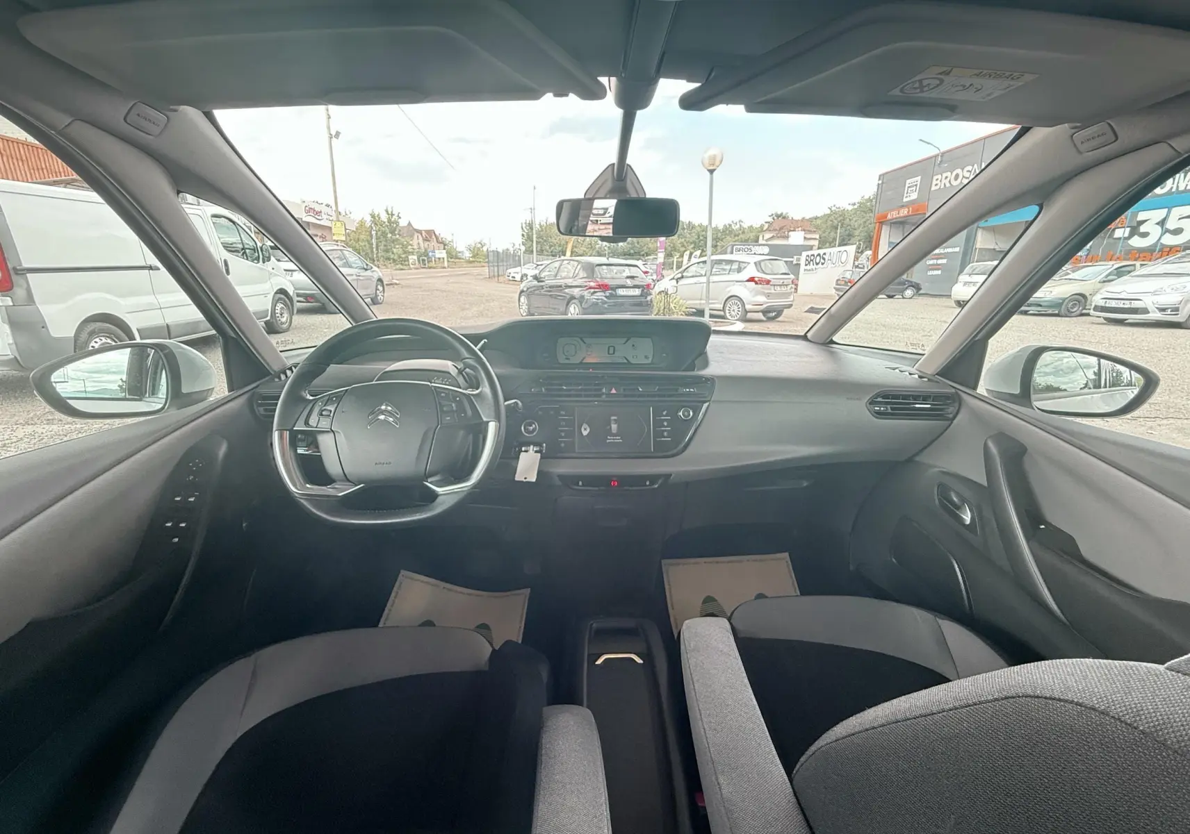 Vue intérieure avant du Citroën C4 Picasso blanc 2014, montrant le tableau de bord et le volant multifonction.