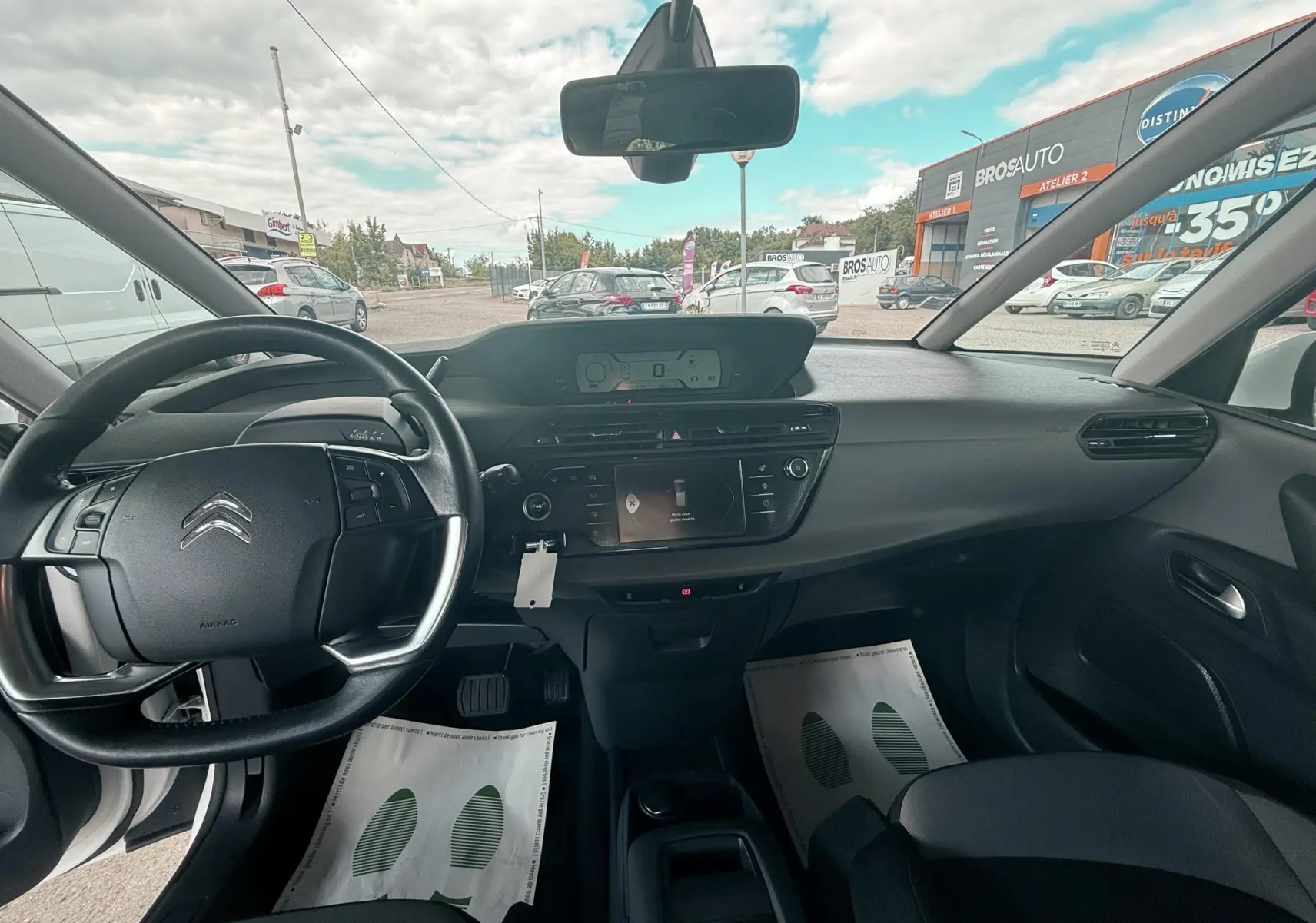 Vue intérieure avant du Citroën C4 Picasso blanc 2014, tableau de bord et volant avec commandes intégrées visibles.