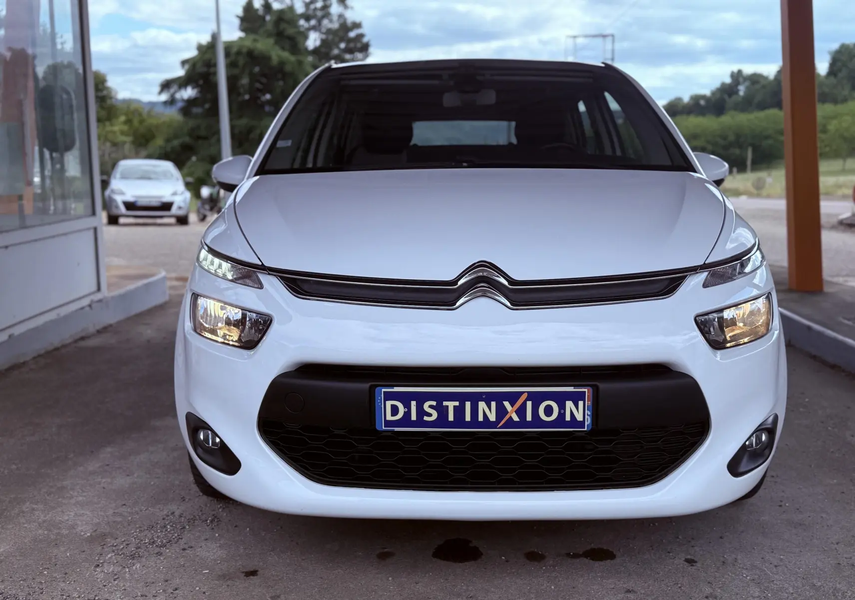 Vue de face d'une Citroën C4 Picasso blanche de 2014 avec phares allumés et calandre noire distinctive.