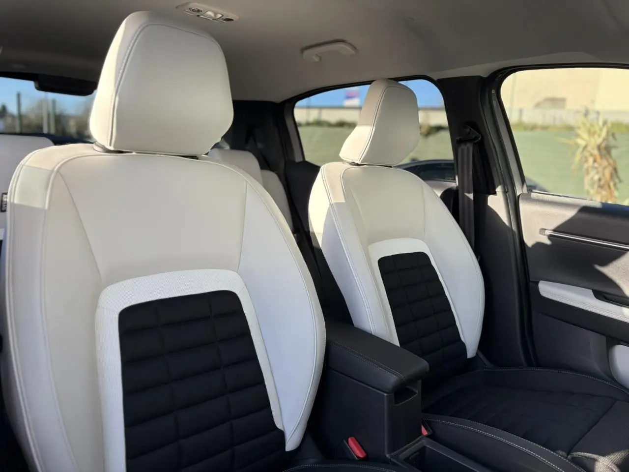 Vue intérieure sur les sièges avant bicolores blanc et noir du Citroën C3 Aircross Hybrid 2025, avec accoudoir central noir.
