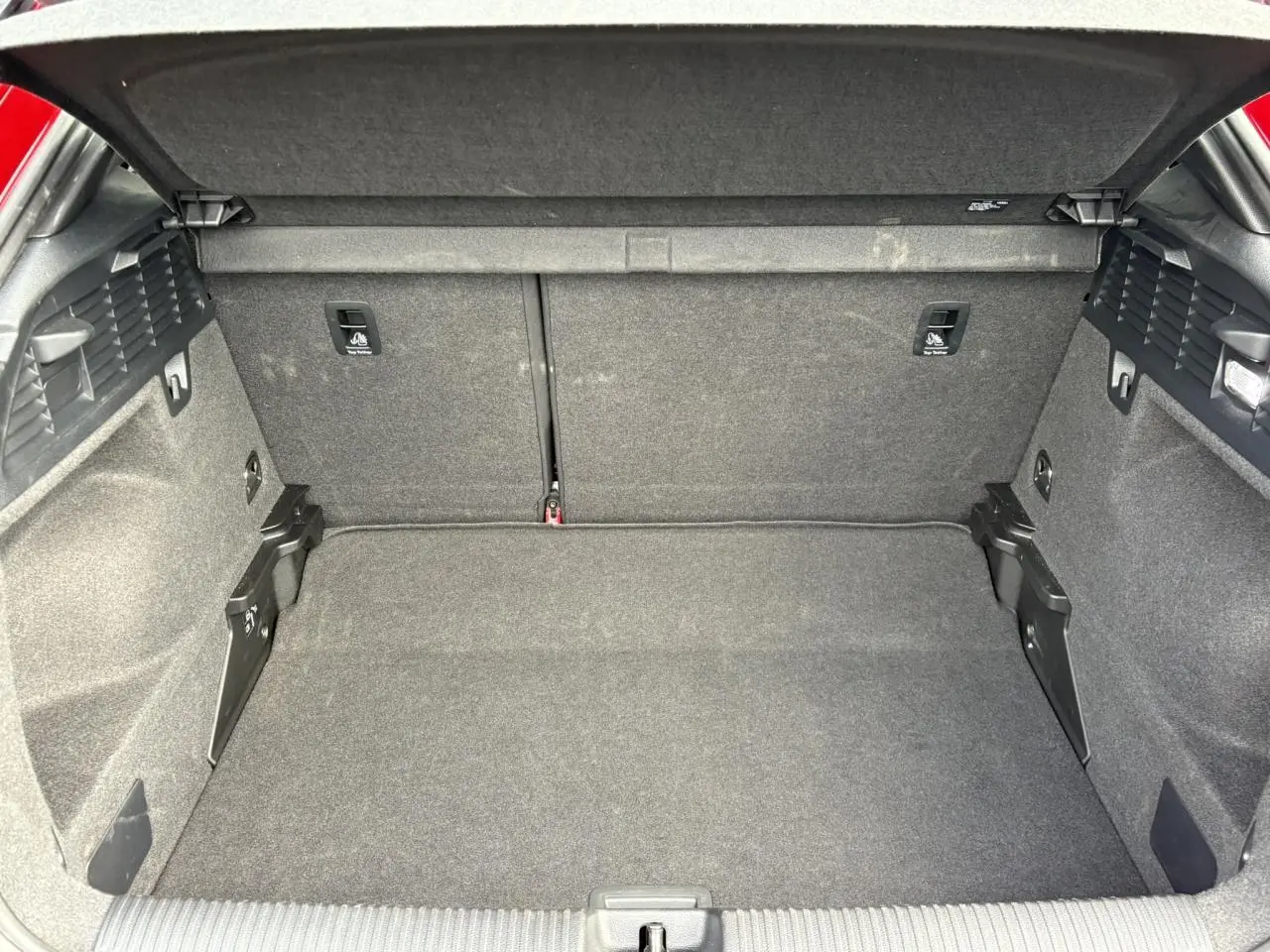 Coffre ouvert d’un Audi Q2 rouge 35 TDI 150 S-Tronic S-Line, montrant l’espace de chargement tapissé de tissu gris.