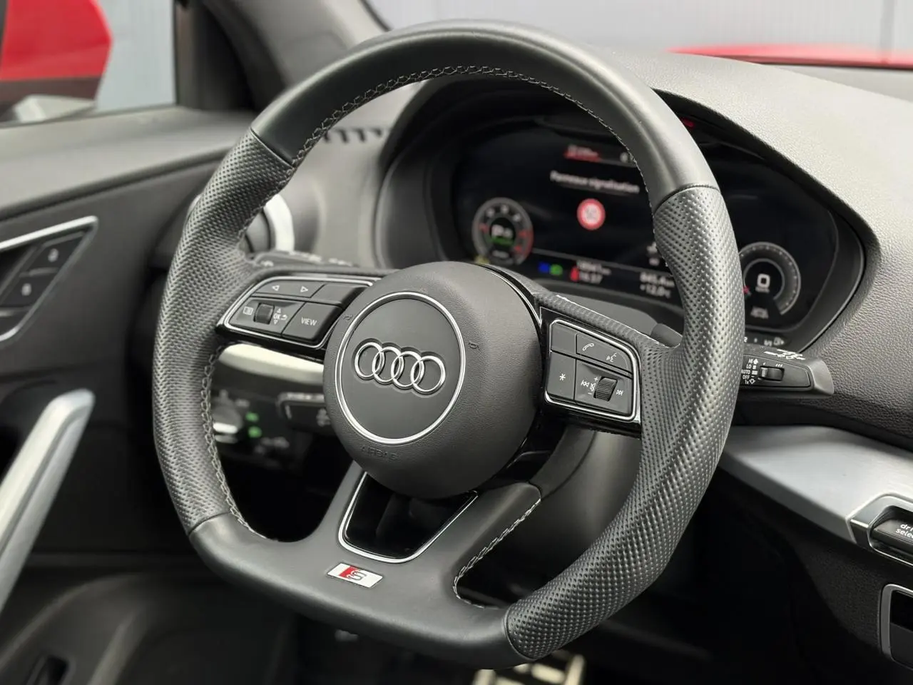 Vue rapprochée du volant cuir perforé S-Line de l'Audi Q2 35 TDI 150, avec tableau de bord numérique en arrière-plan.