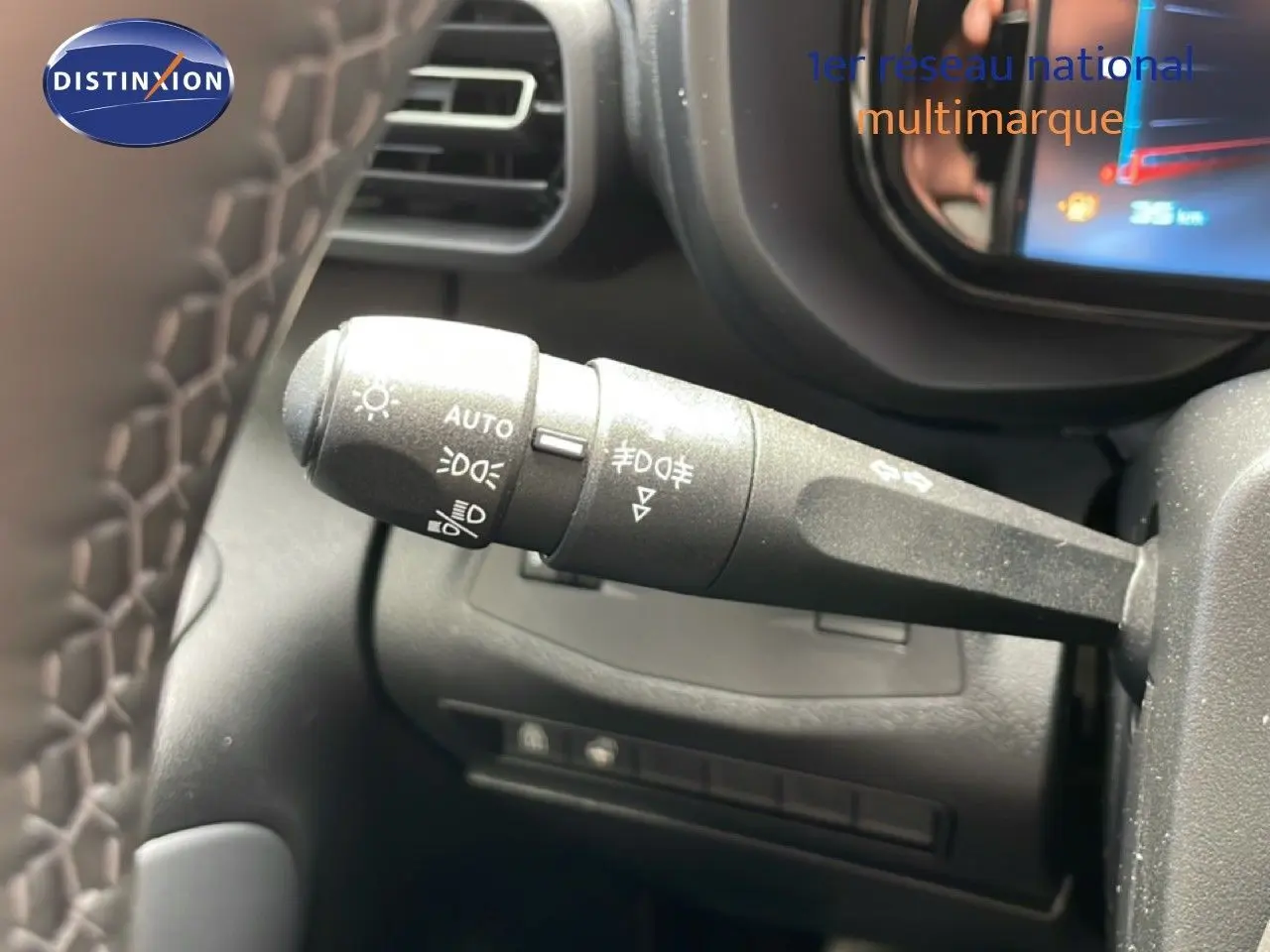 Gros plan sur la commande des feux au volant du Citroën Berlingo gris, avec tableau de bord numérique en arrière-plan.