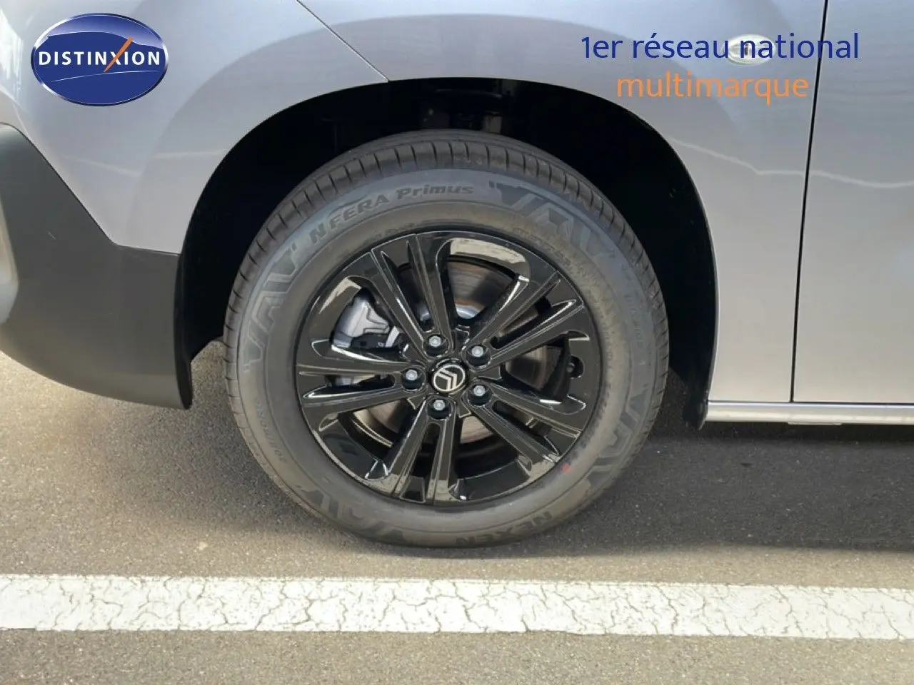 Gros plan sur la roue avant gauche noire brillante d’un Citroën Berlingo gris Artense Metal, avec partie de la carrosserie visible.