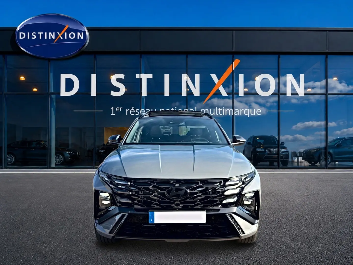 Vue avant d'un Hyundai Tucson gris shadow 2026 avec calandre noire et toit panoramique devant un showroom Distinxion.