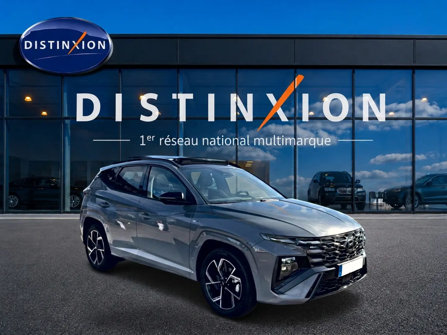 Hyundai Tucson gris shadow en 3/4 avant droit, avec jantes alu et toit panoramique en verre visible.
