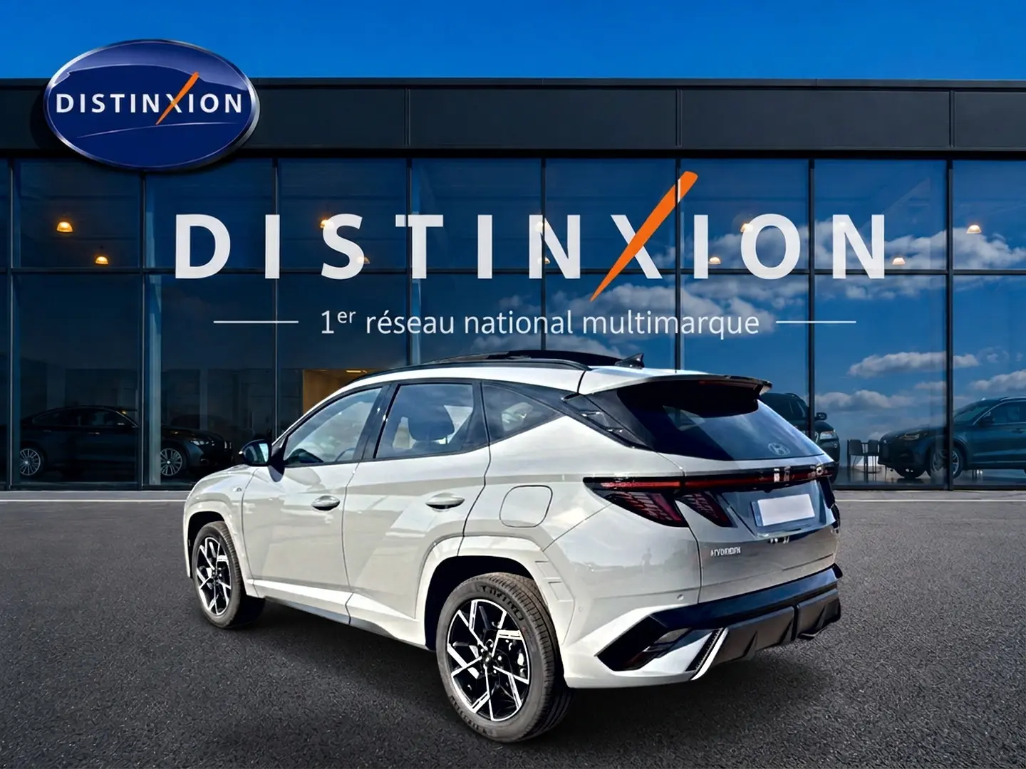 Vue 3/4 arrière du Hyundai Tucson gris shadow avec jantes alu noires et toit panoramique, devant une vitrine Distinxion.
