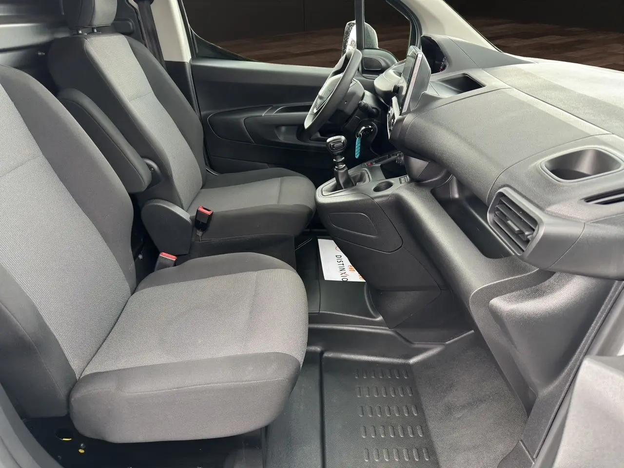 Intérieur du Peugeot Partner 2022 vu côté conducteur, sièges tissu gris et tableau de bord noir avec boîte manuelle.