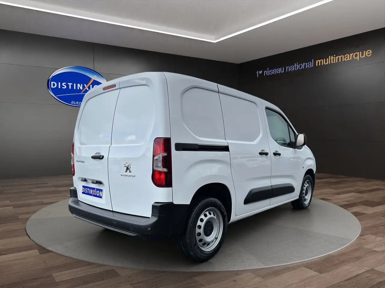 Peugeot Partner blanc en 3/4 arrière droit, utilitaire compact avec portes arrière battantes et protections latérales noires.