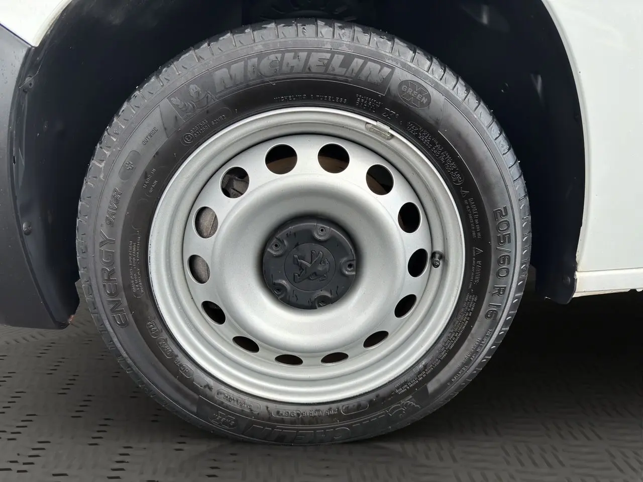 Gros plan sur la roue avant gauche du Peugeot Partner blanc 2022, pneu Michelin Energy Saver avec jante acier grise.