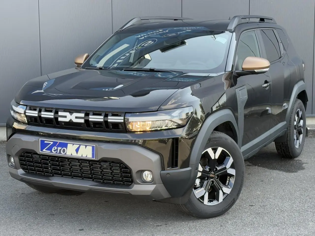 Vue 3/4 avant droite d'un Dacia Duster 2025 noir nacré avec coques de rétroviseur cuivrées et jantes alliage 17 pouces.