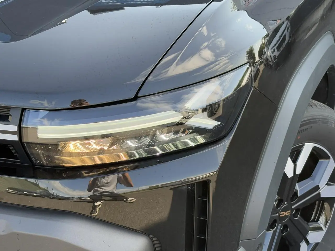 Gros plan sur le phare avant droit et la jante alliage du Dacia Duster noir nacré 2025 finition Extrême.