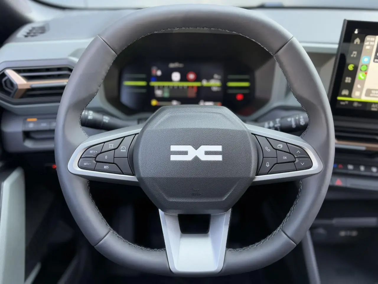 Vue rapprochée du volant noir du Dacia Duster 2025 avec commandes intégrées et tableau de bord digital en arrière-plan.