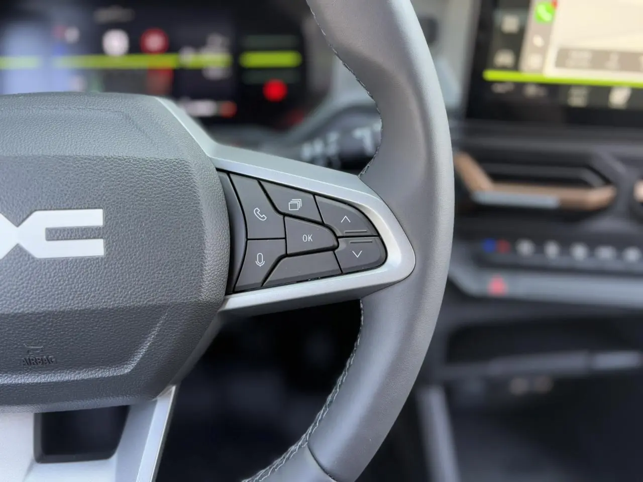 Gros plan sur le volant cuir noir du Dacia Duster 2025, avec commandes multifonctions et tableau de bord flou en arrière-plan.