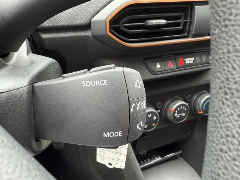 Gros plan sur la commande audio au volant d'une Dacia Sandero Stepway bleu métal 2022, avec tableau de bord noir et orange.