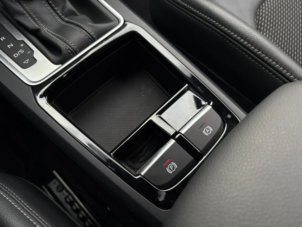 Gros plan sur la console centrale de l'Audi Q2 35 TDI S-Line 2025, montrant la boîte auto et les commandes de frein à main électrique.