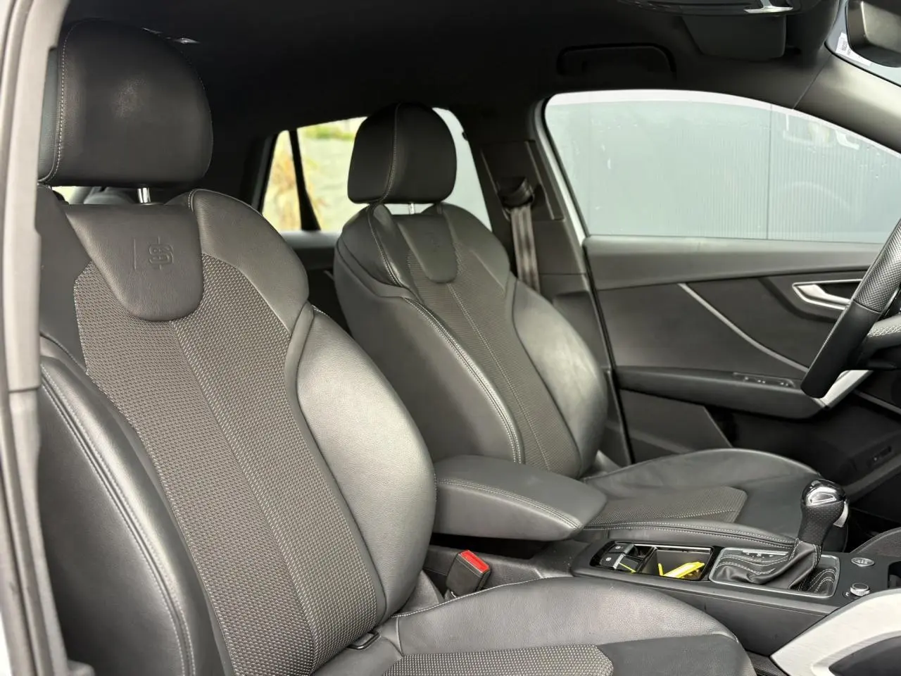 Vue intérieure côté conducteur de l'Audi Q2 S-Line 35 TDI 150 avec sièges sport cuir/tissu noirs et console centrale.
