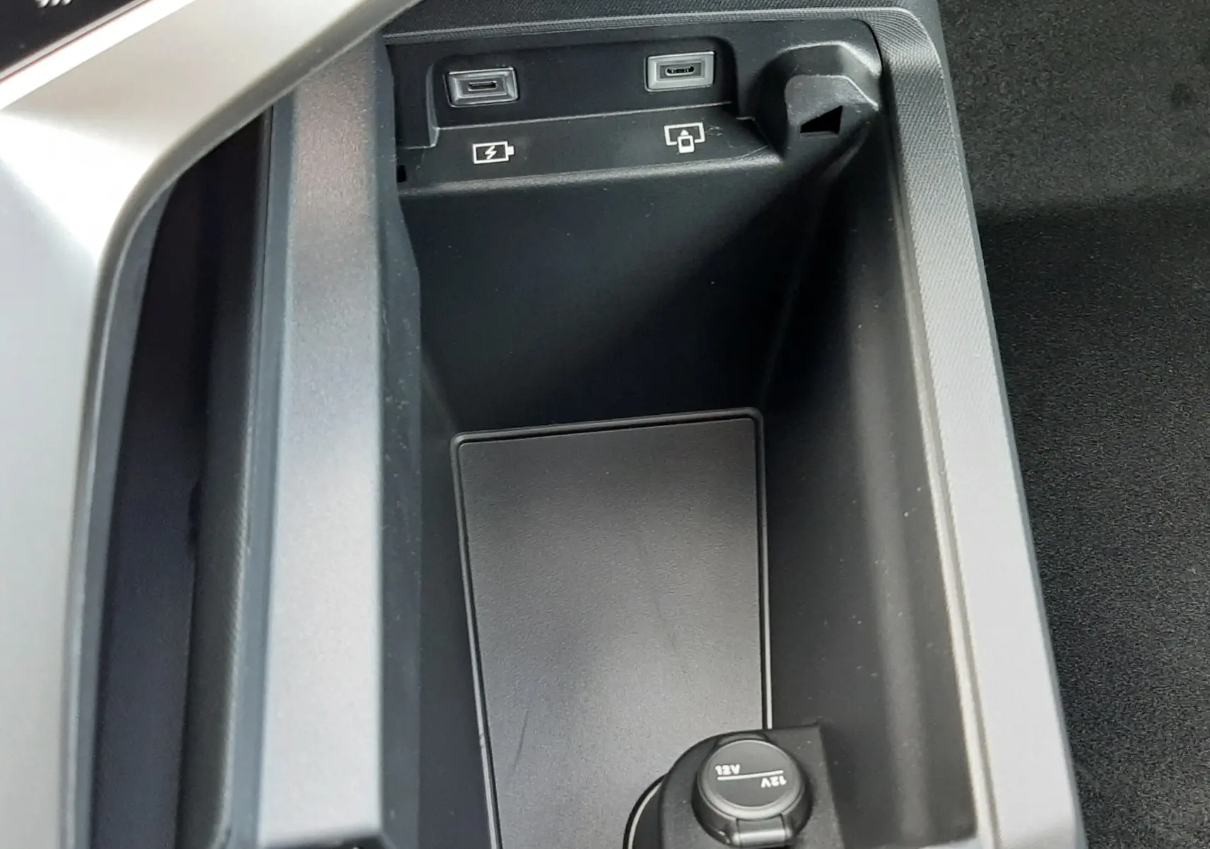 Vue rapprochée de la console centrale noire du Peugeot 3008 hybride 2026, montrant les ports USB et prise 12V.
