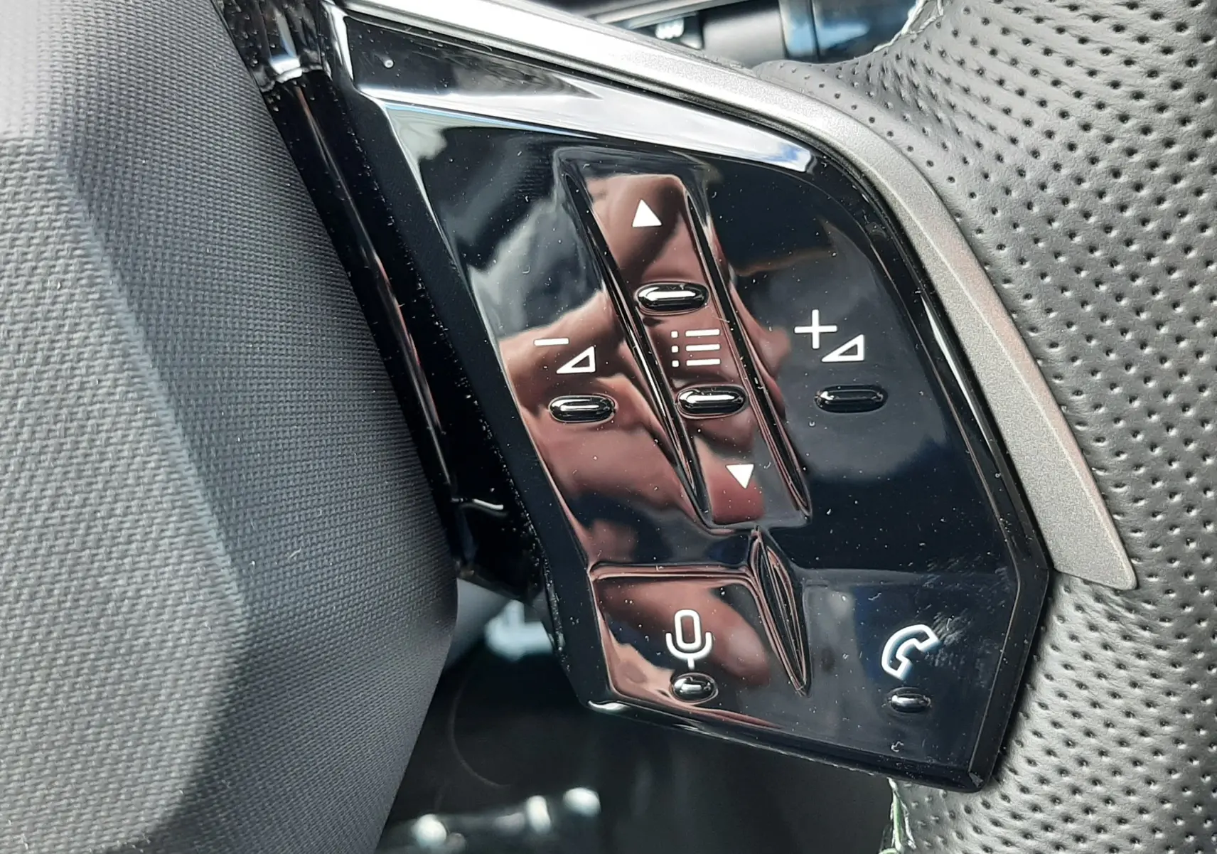 Gros plan sur les commandes multifonctions noires à gauche du volant perforé du Peugeot 3008 gris titane 2026.