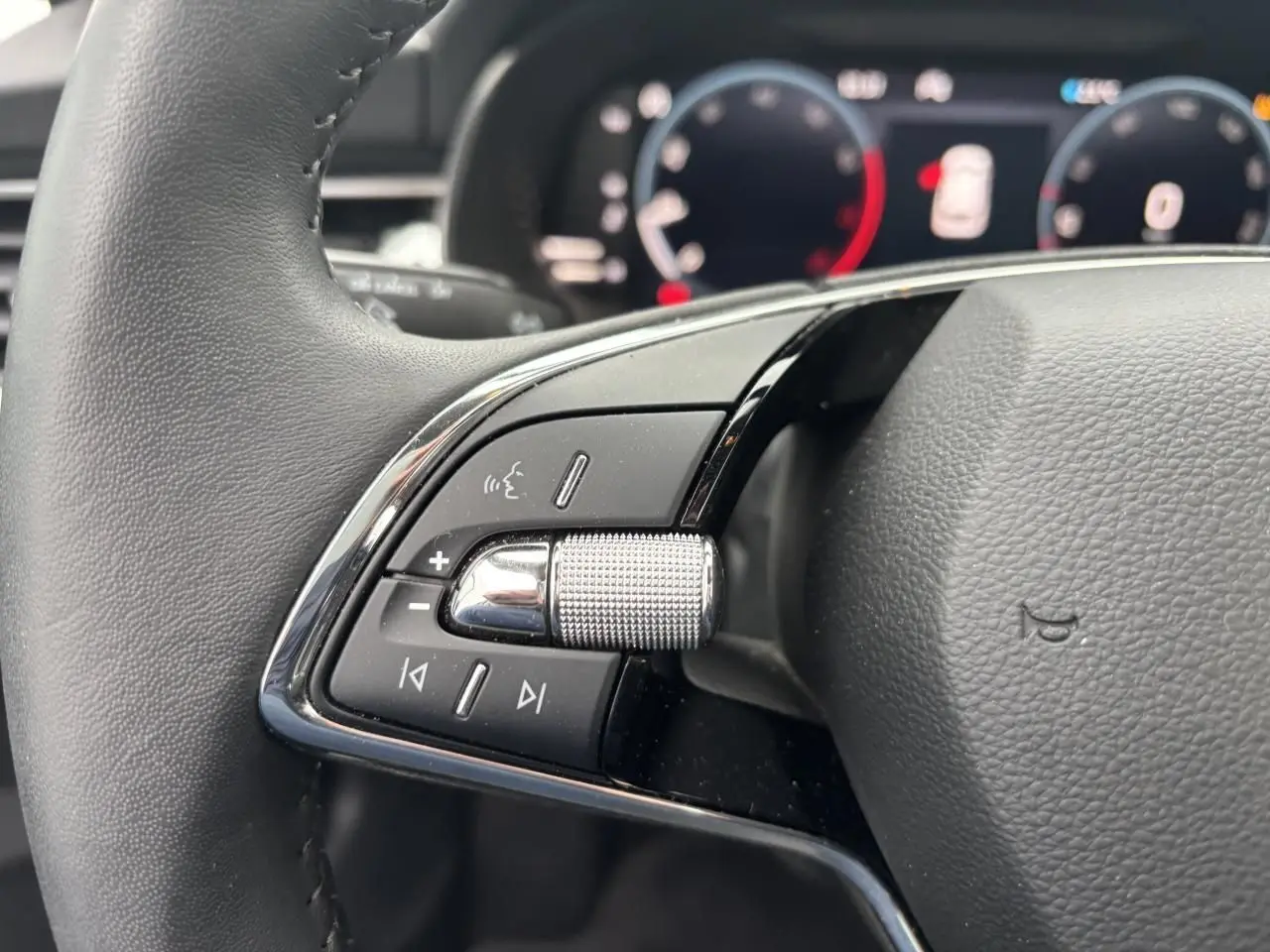 Gros plan sur le volant cuir à deux branches du Skoda Kamiq 2024, avec commandes audio et molette texturée côté gauche.