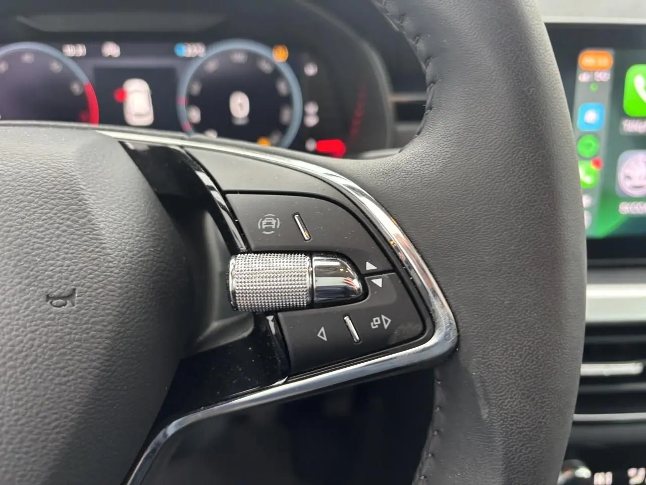Gros plan sur le volant cuir 2 branches du Skoda Kamiq 2024, avec commandes multifonctions et tableau de bord numérique flou.